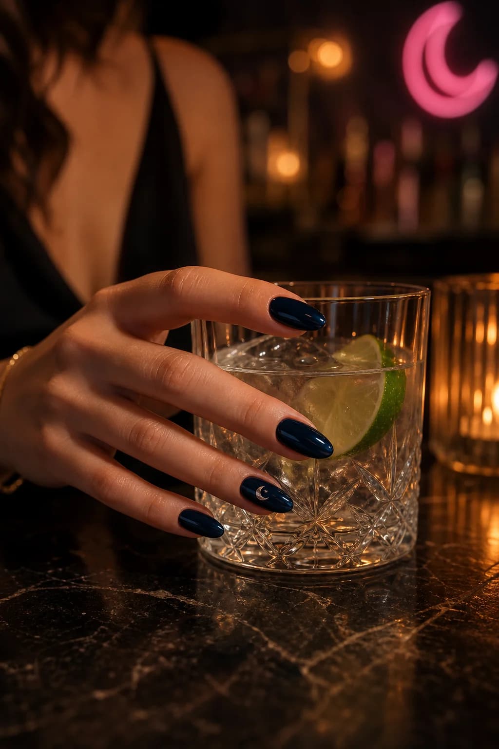 Navy almond nails holding a glass; one nail wears the Vesper crescent sticker