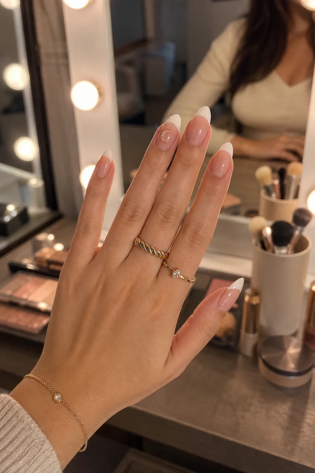 Almond french-tip nails with the Vesper crescent sticker in front of a vanity mirror
